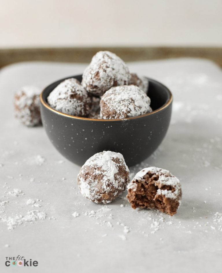 Vegan Eskimo kisses cookies in a black bowl with more cookies and powdered sugar surrounding it.