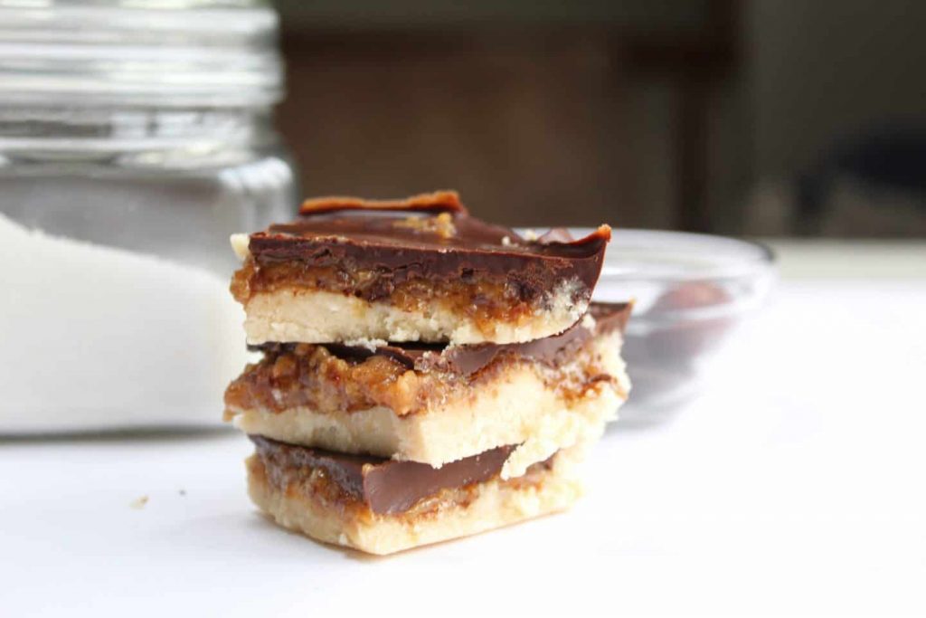 Layed, square Millionaire Shortbread stacked next to a jar of sugar.