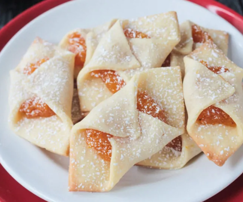 Folded Kolaczki cookies with apricot jam in the middle and a dusting of powdered sugar.