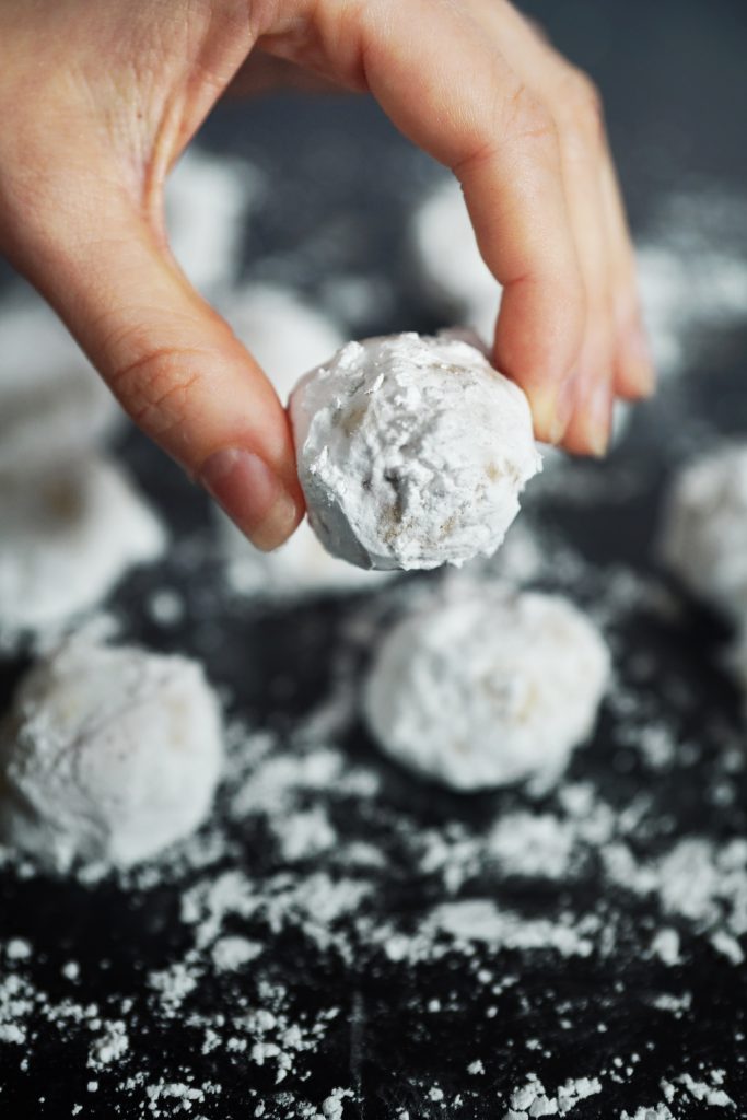 hand holding a single round Italian butterball cookie covered in powdered sugar with others in the background.