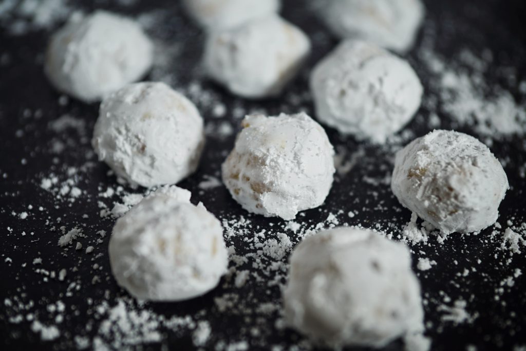 A close up of round Italian butterball cookies covered in powdered sugar on a black tray.