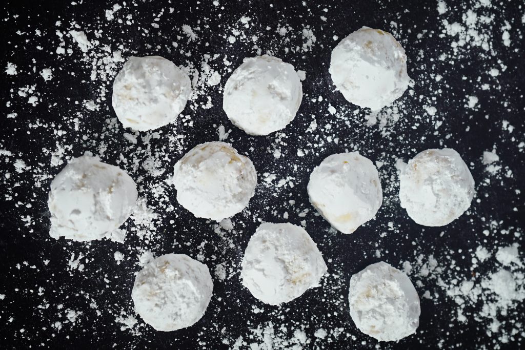 Flatlay of butterball cookies on a black tray dusted with powdered sugar.