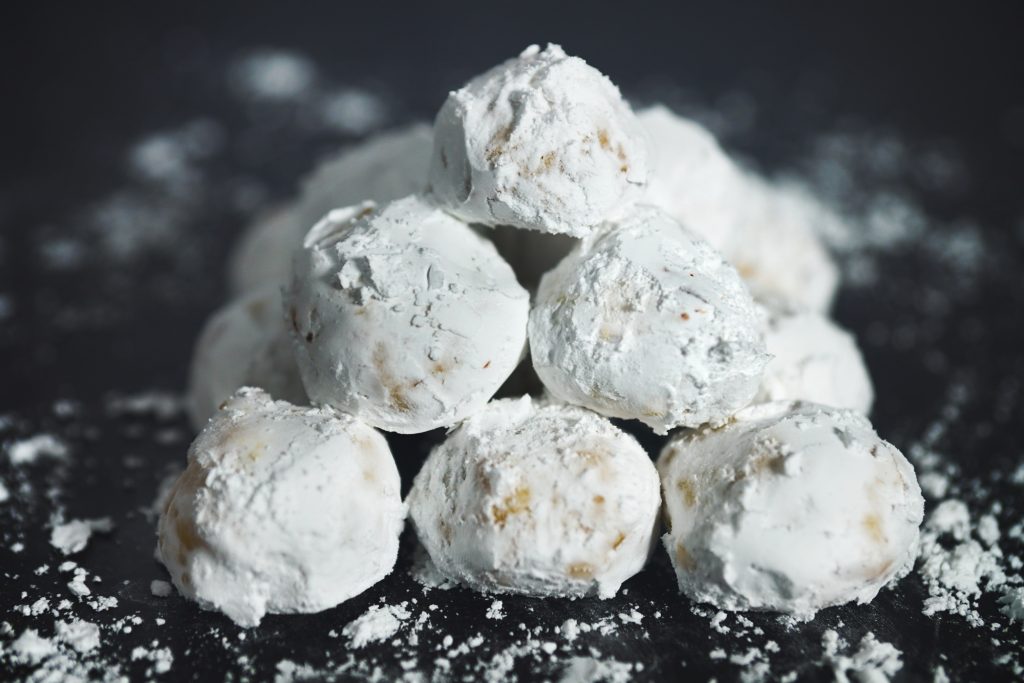 Round butterball cookies coated in powdered sugar on a black counter.