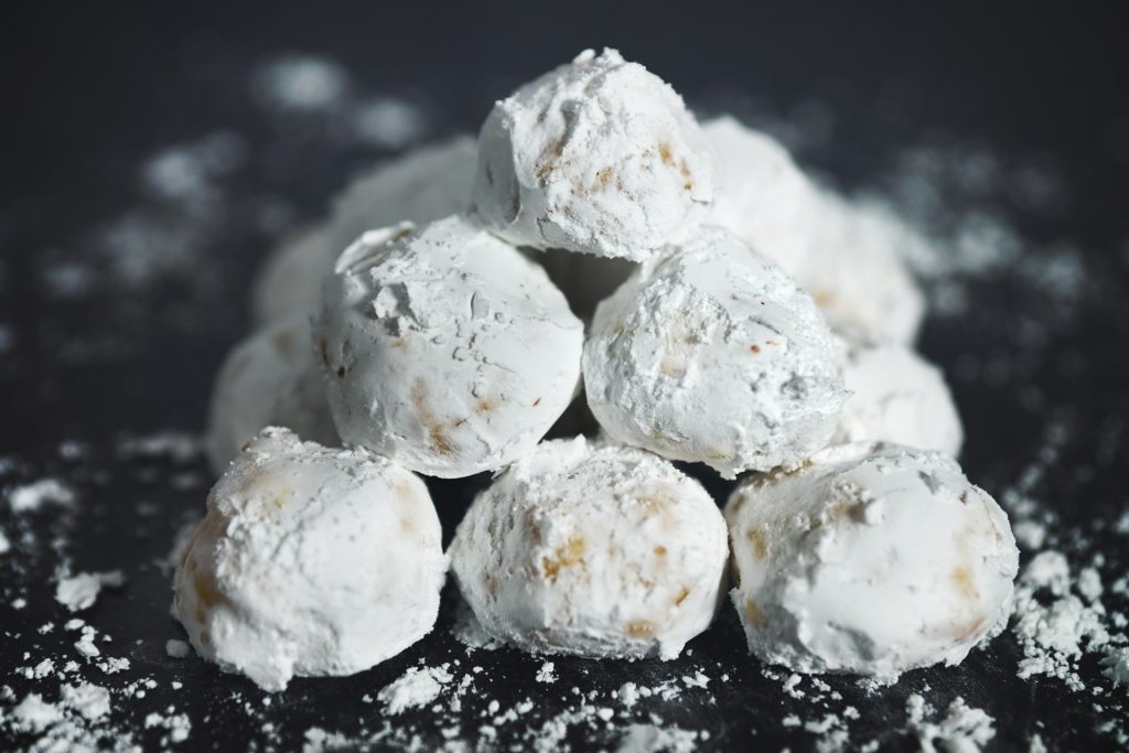 Round Italian butterball cookies covered in powdered sugar stacked in a pyramid on black counter.