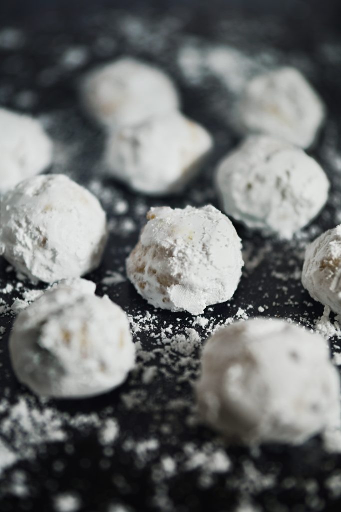 Round Italian butterball cookies covered in powdered sugar on a black countertop.