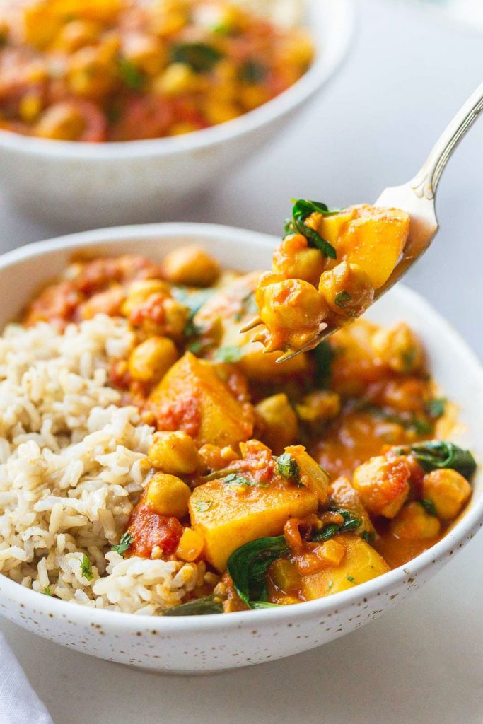 Photo of chickpea and potato curry being served in a white bowl. 