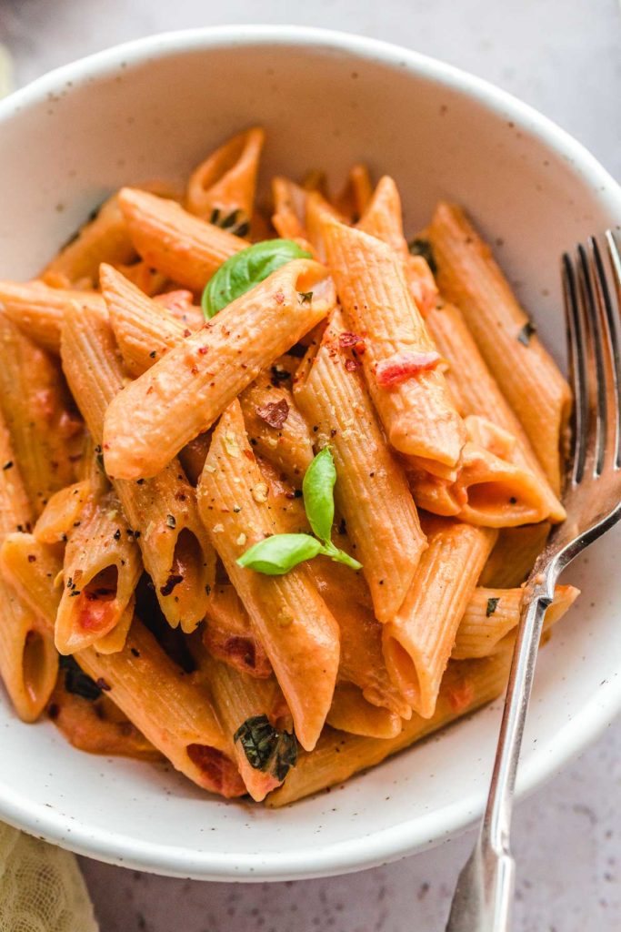 Photo of creamy tomato pasta being served in a white bowl. One of the amazing vegan recipes for kids.