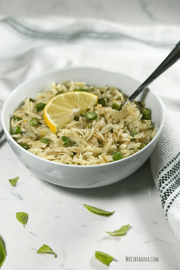 Photo of a white bowl with lemon orzo inside topped with a lemon wedge. 