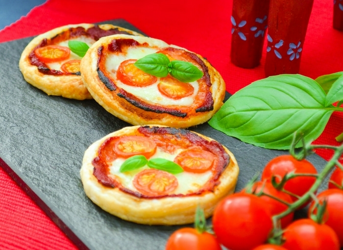 Photo of Mini Margherita Puff Pizza Pies. 3 mini margherita pizzas are seen on a slate board with a red table cloth underneath. One of the many vegan recipes for kids.