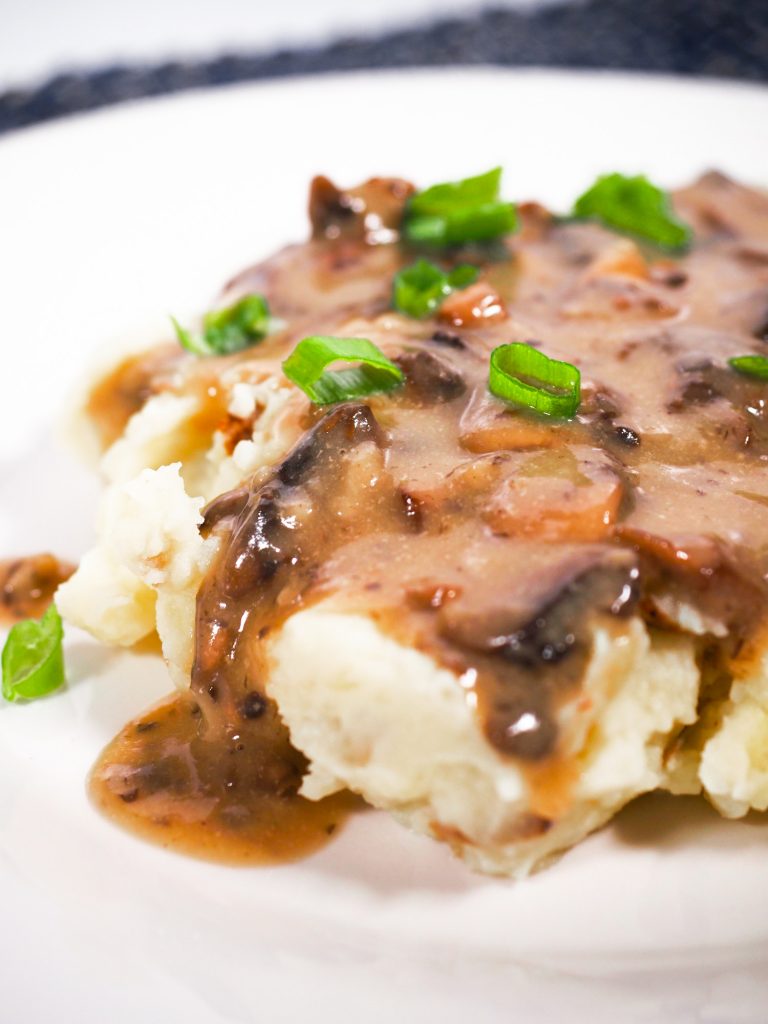 close up of vegan brown gravy with mushrooms over mashed potatoes