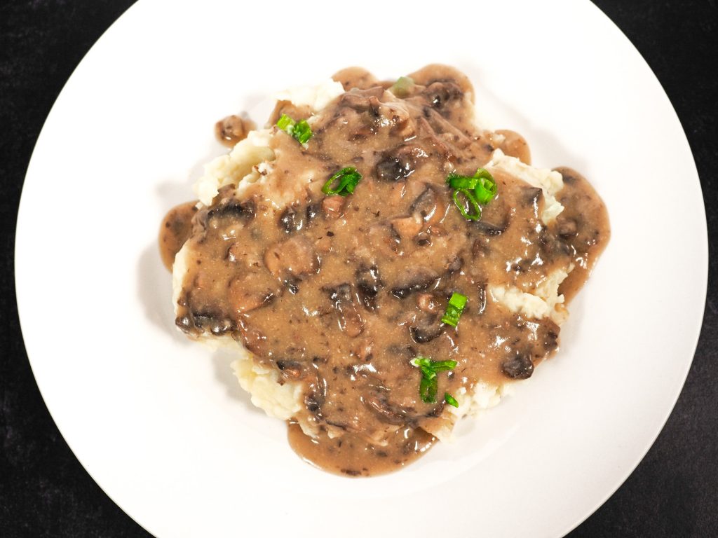 Flatlay of delicious vegan mushroom gravy over potatoes on white plate.