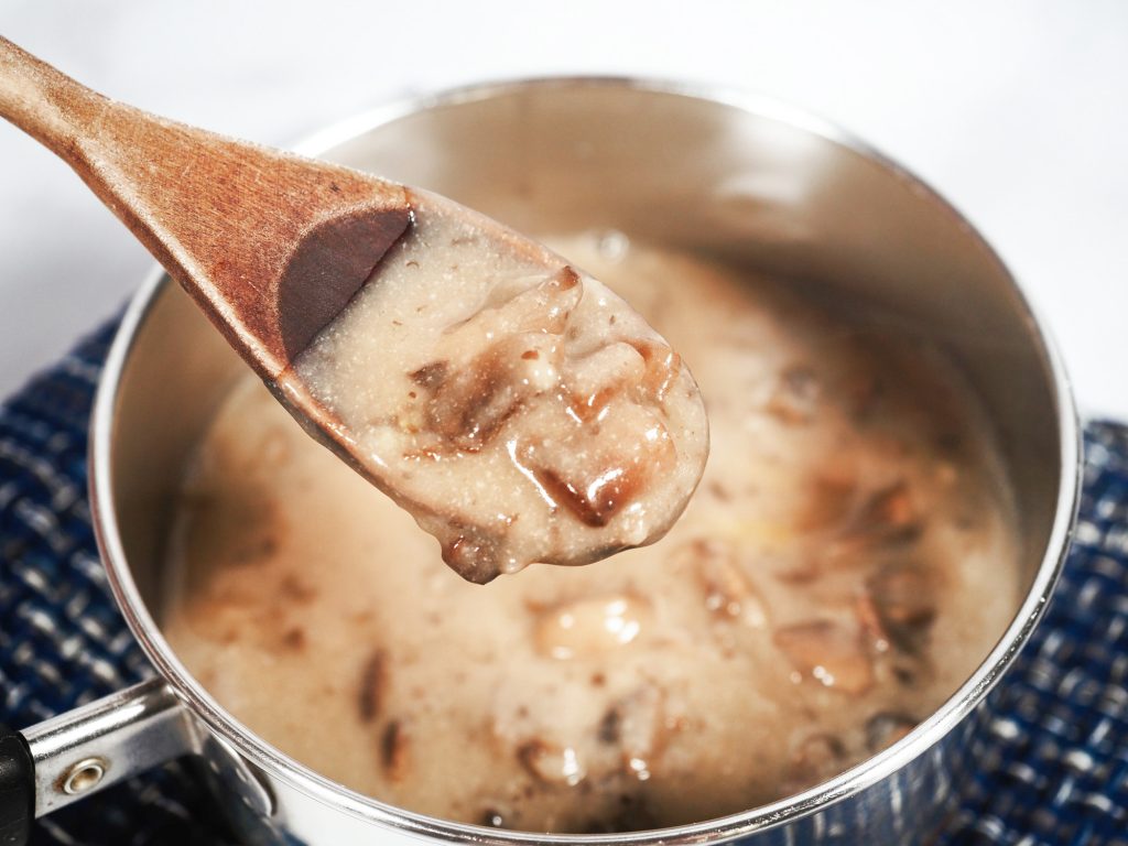 Spoon lifting from a pot of chopped mushrooms in gravy