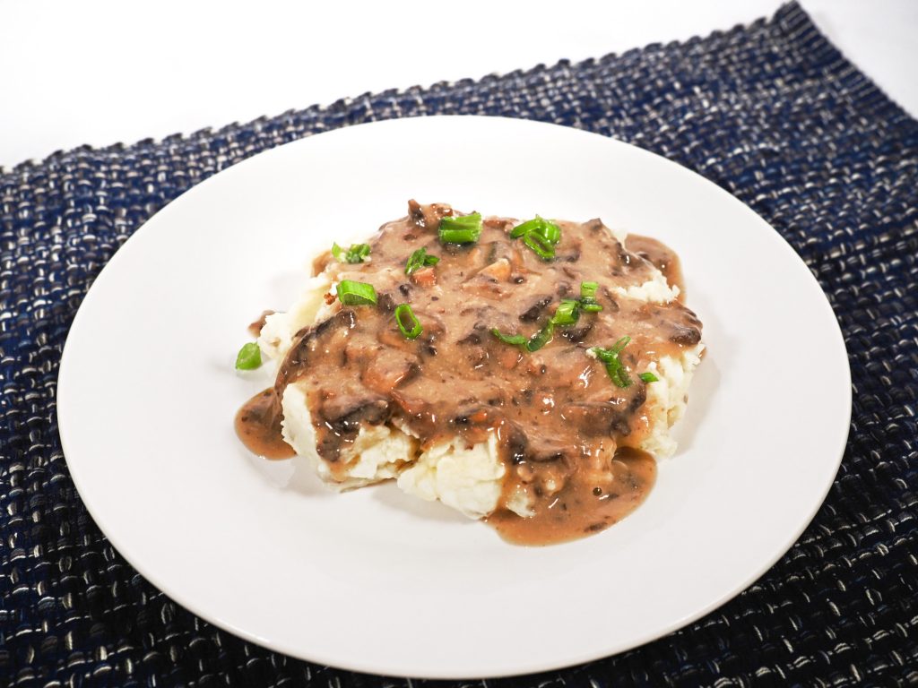 brown vegan gravy with mushrooms on mashed potatoes on a white plate.