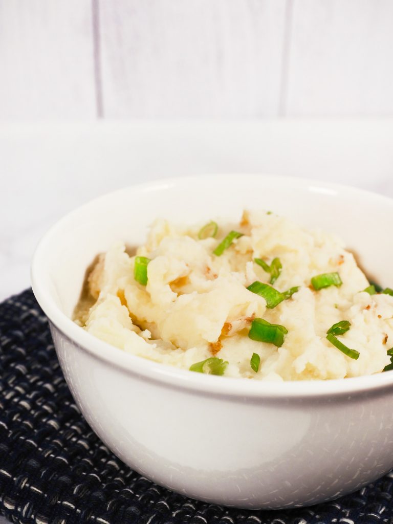 close up of white mashed potatoes in a bowl with green scallions on top of it