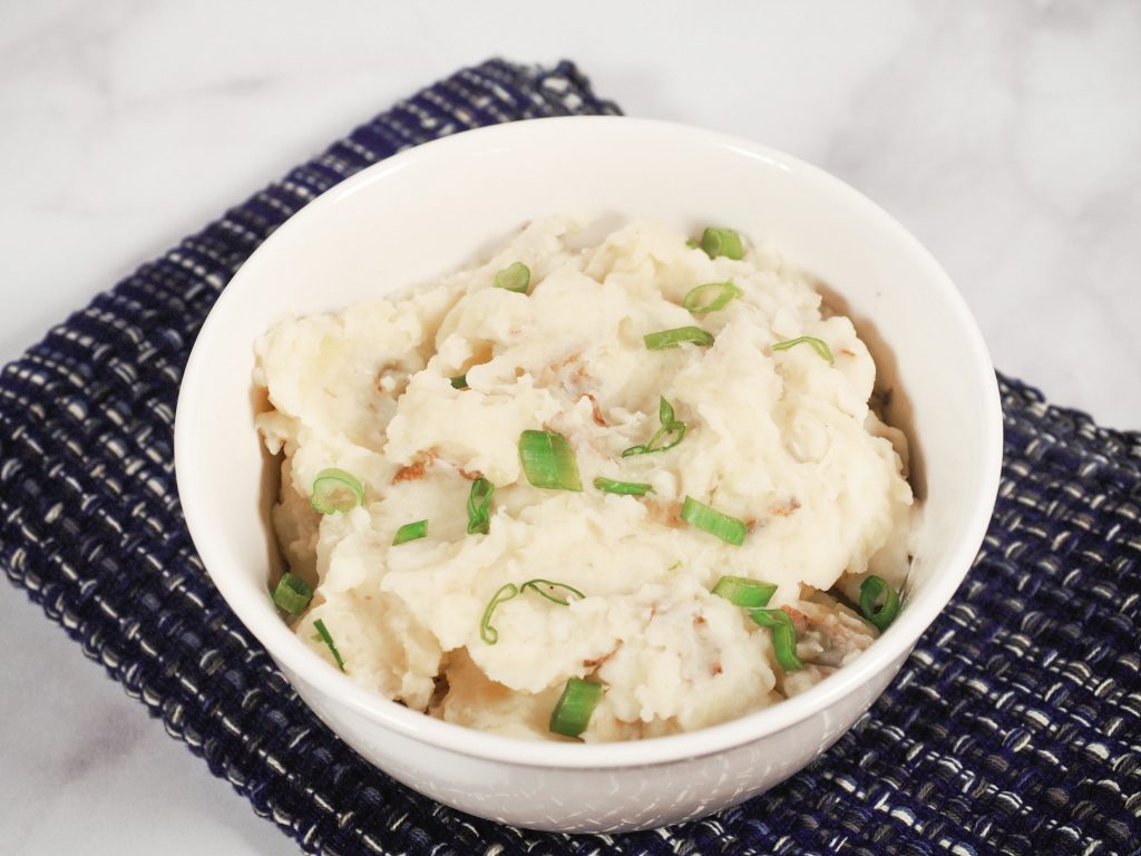 healthy mashed potatoes with green onions in a white bowl on top of a blue towel