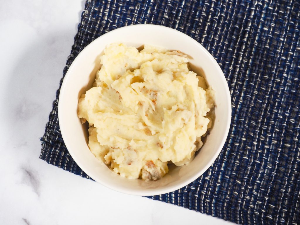creamy vegan mashed potatoes with skin on in bowl on top of blue place mat