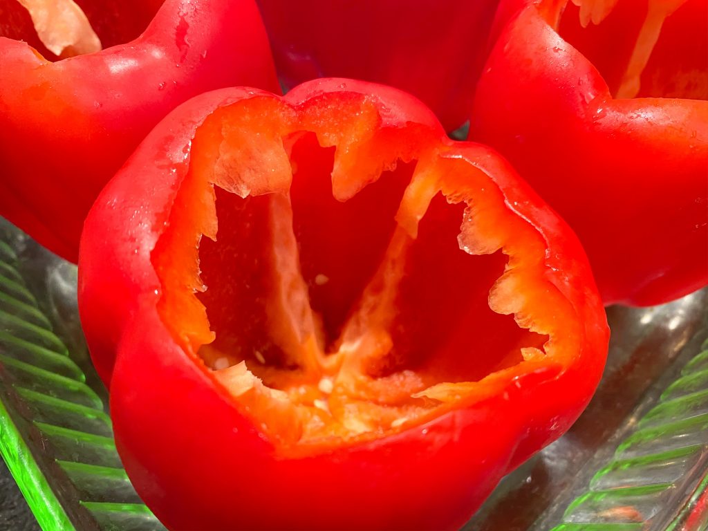 Close-up of raw red bell peppers cored in dish.