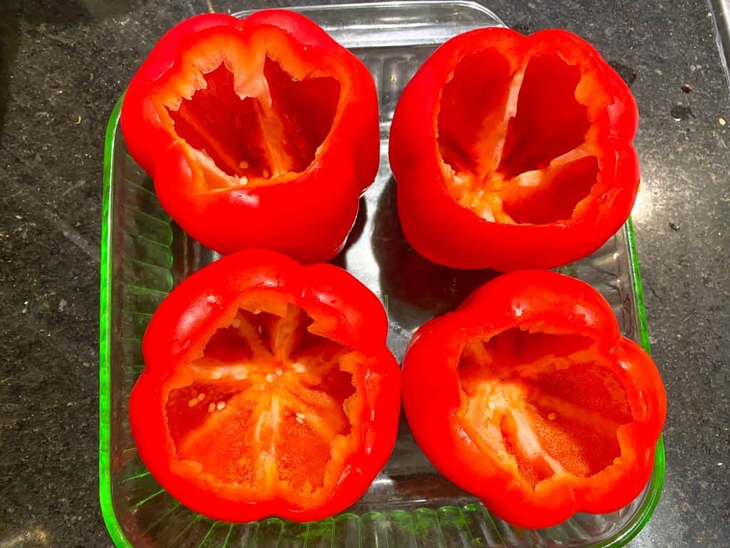 Four raw red bell peppers cored in baking dish.