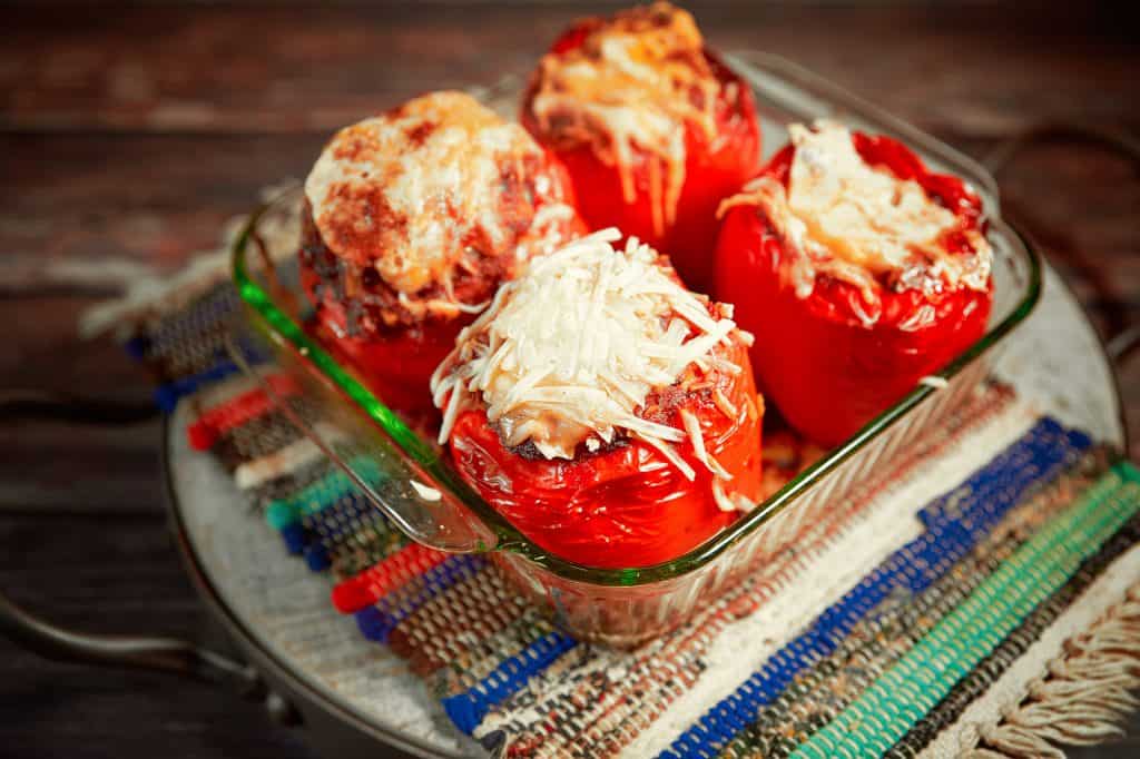 Four red bell peppers stuffed with vegan cheese and baked in dish on a colorful mat.