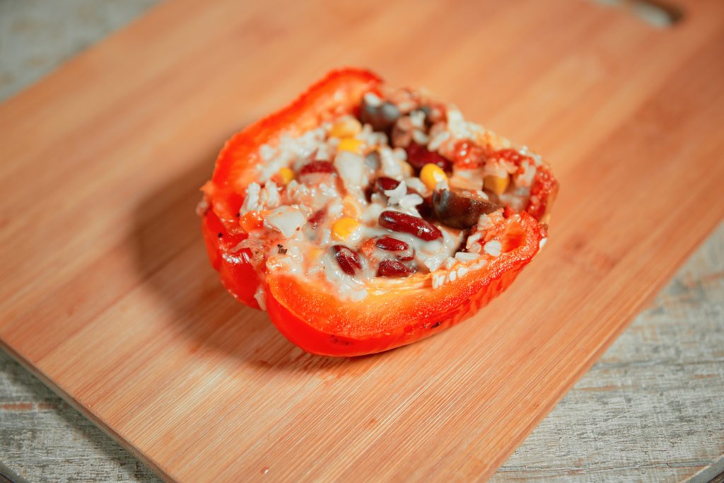 Single stuffed red bell pepper sliced in half on a wooden cutting board demonstrating how to eat it.