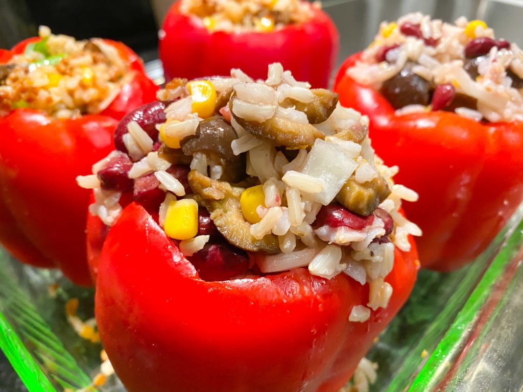 Close up of four plant based, red stuffed peppers ready for cooking.