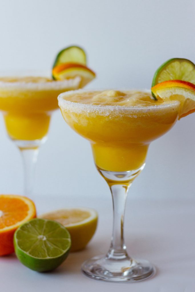 Photo of two fresh citrus margaritas with lemon, orange, and lime slices as a garnish next to cut citrus.
