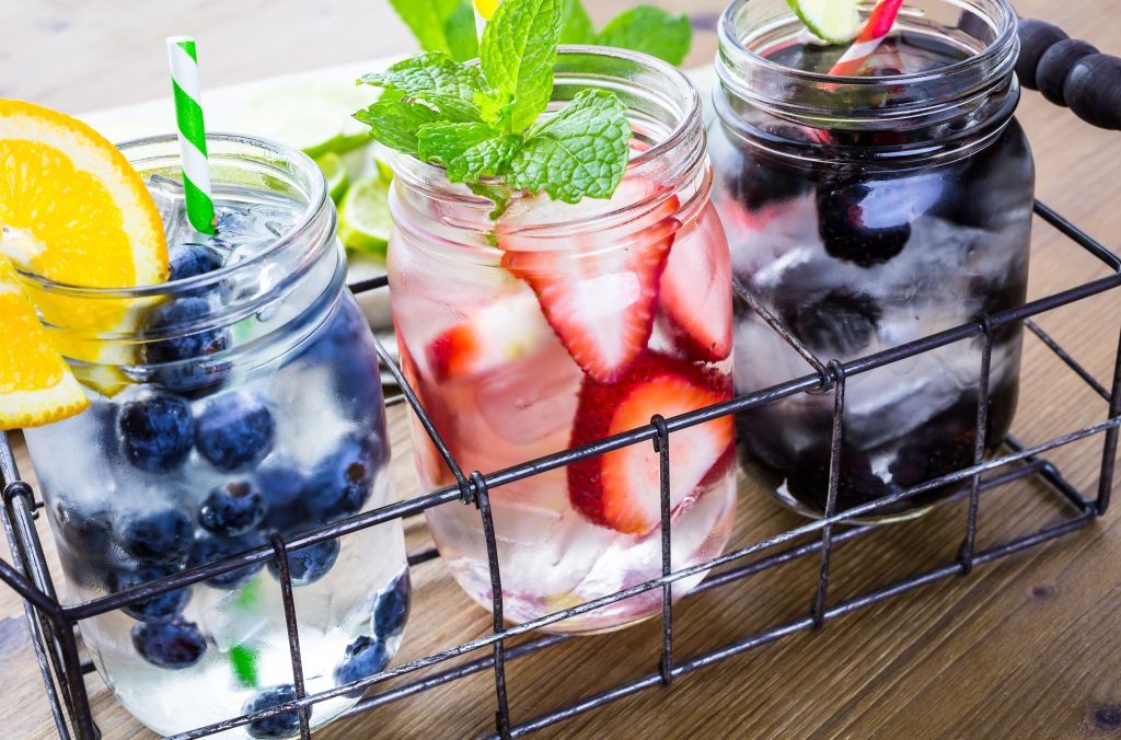 Photo of three clear cocktails with fruit and a garnish served in mason jars.