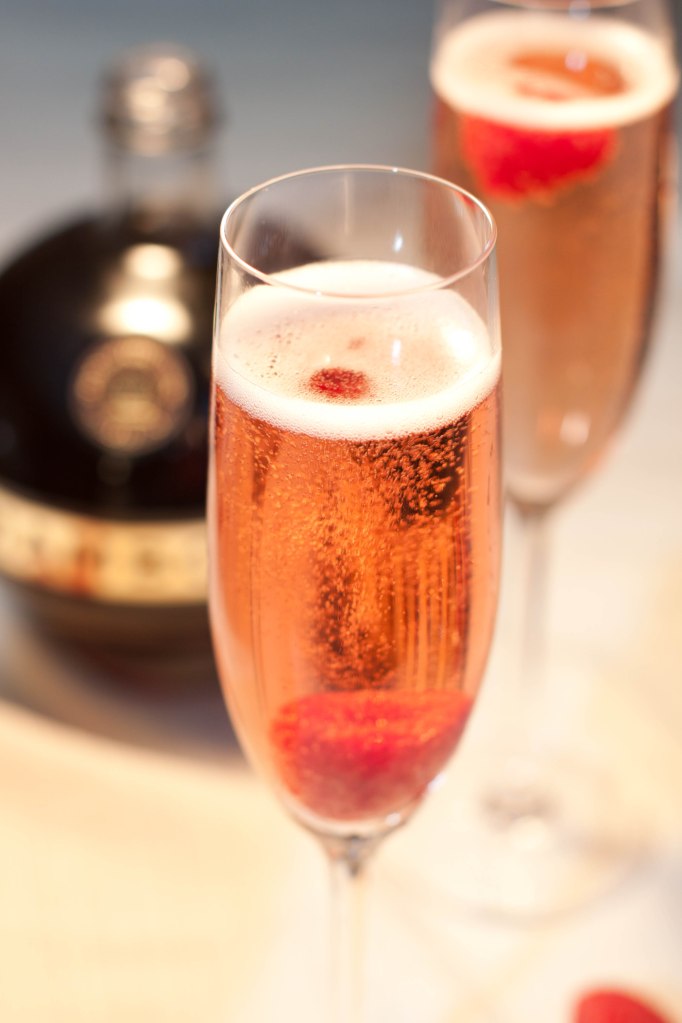 Close up photo of a champagne flute serving a french kiss cocktail with a raspberry garnish.
