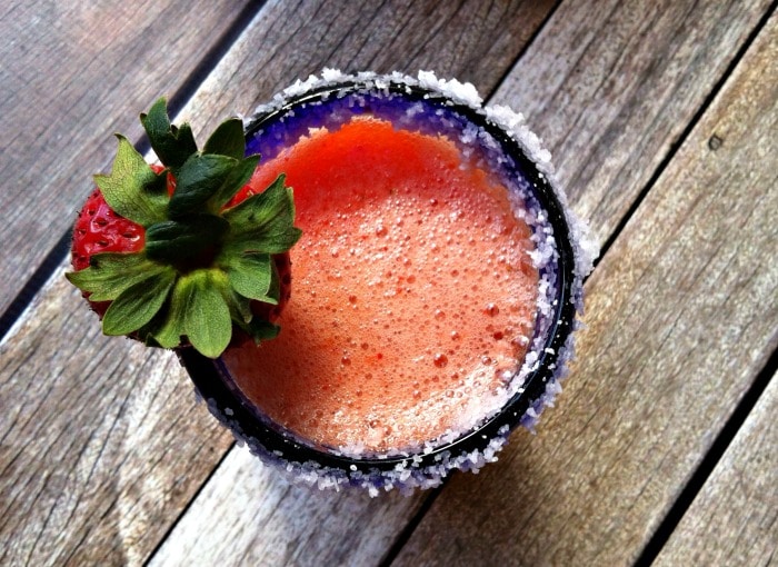 Straight down view of a blue glass serving a strawberry mango margarita with a salted rum and a strawberry garnish.