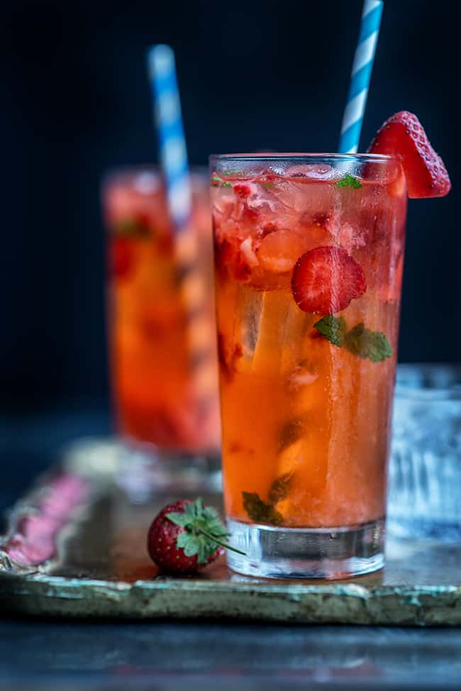 Photo of two tall glasses serving strawberry Moscow mule with a strawberry garnish.