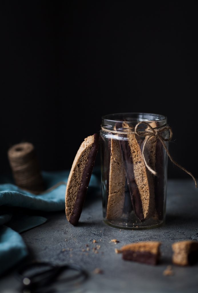 Photo of an open glass jar filled with Vegan Chocolate Dipped Olive Oil Biscotti. 