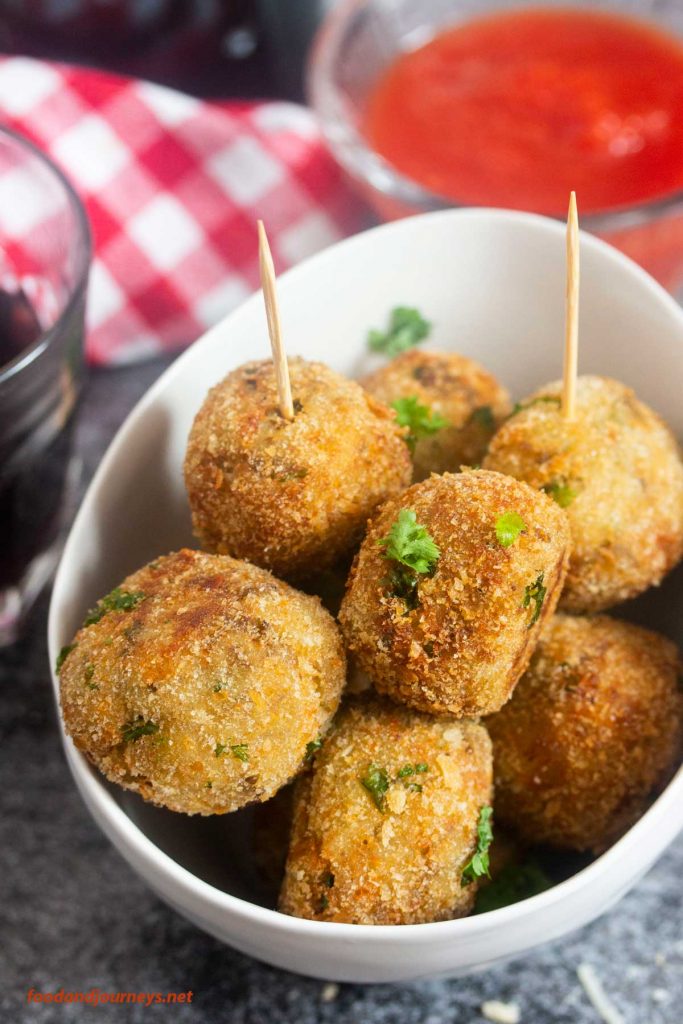 Photo of a deep bowl serving Neapolitan eggplant meatballs with toothpicks. A small bowl of red sauce is seen in the background.