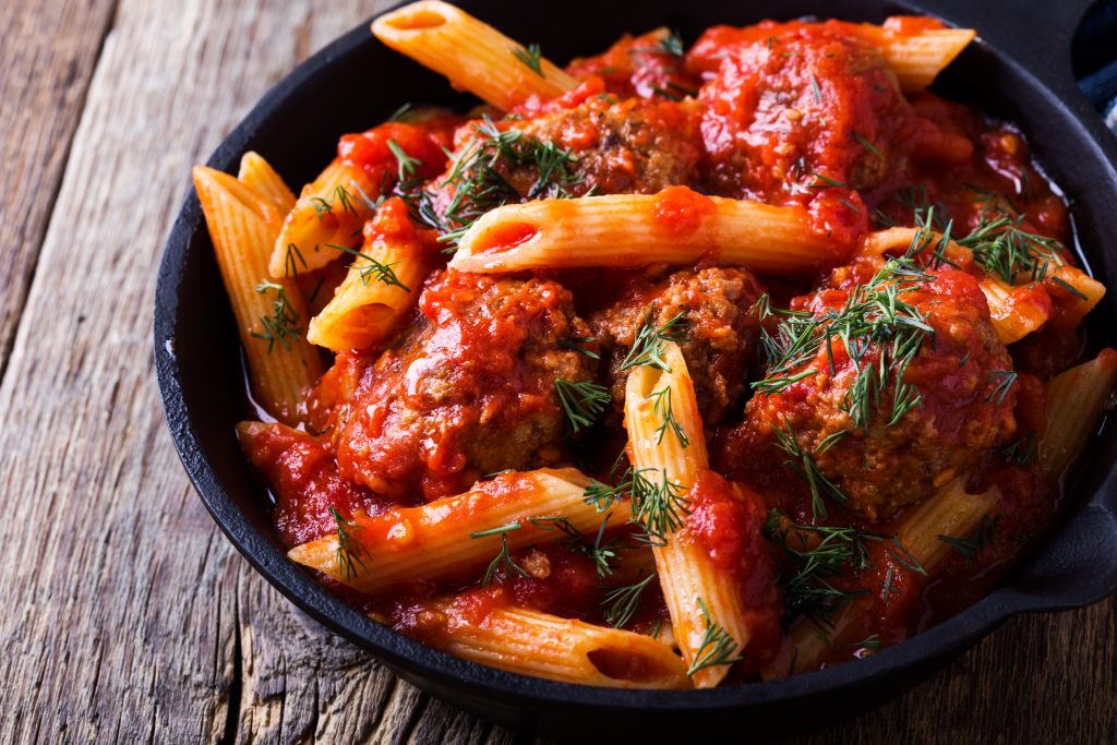 Photo of penne pasta with red sauce being served in a cast iron skillet.