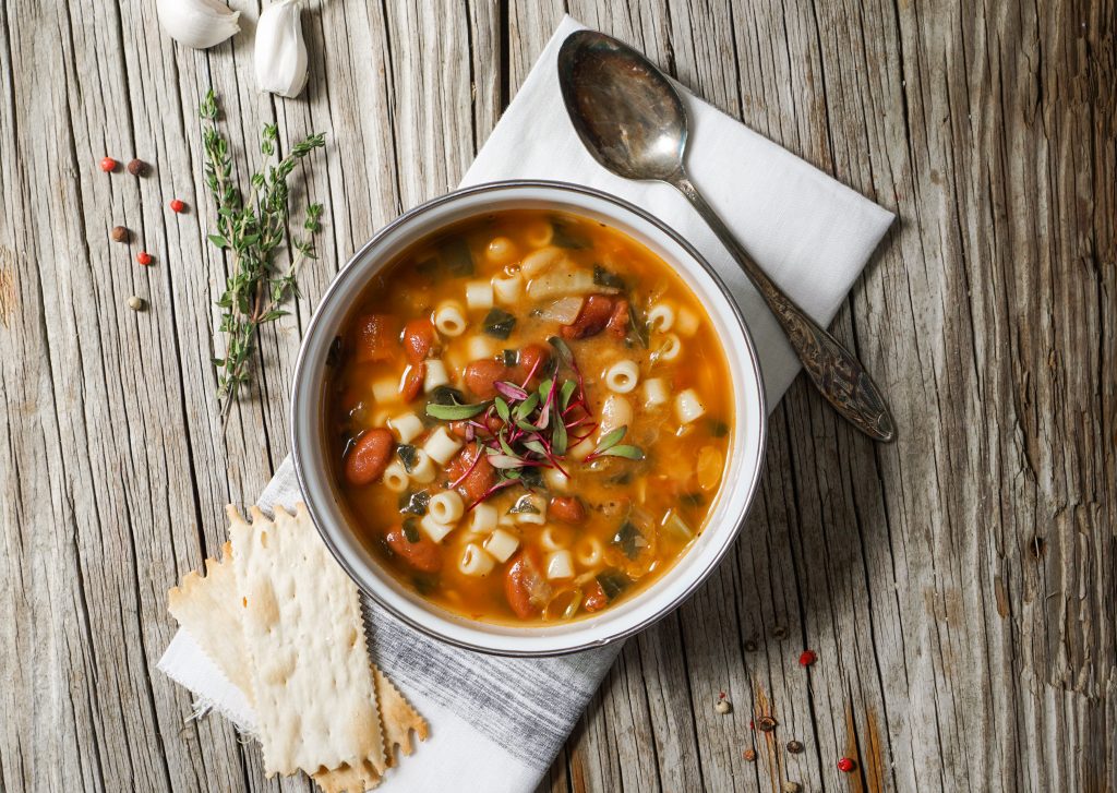 Photo of minestrone soup on a rustic wooden table with a cloth napkin.