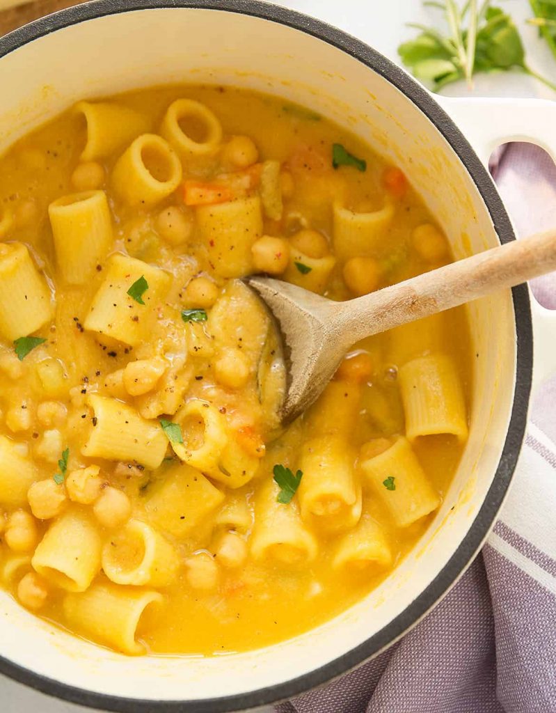 Photo of a pot serving pasta with chickpeas with a wooden spoon. A comforting staple among the vegan Italian recipes.