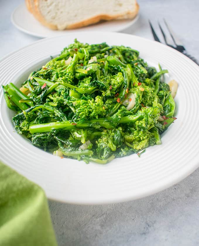 Photo of bright green rapini being served in a white round bowl. 
