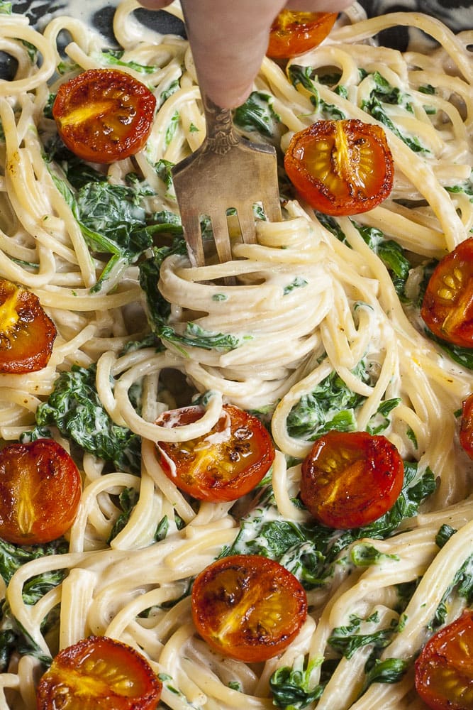 Photo of vegan Alfredo sauce being served with spaghetti, spinach, and cherry tomatoes. 