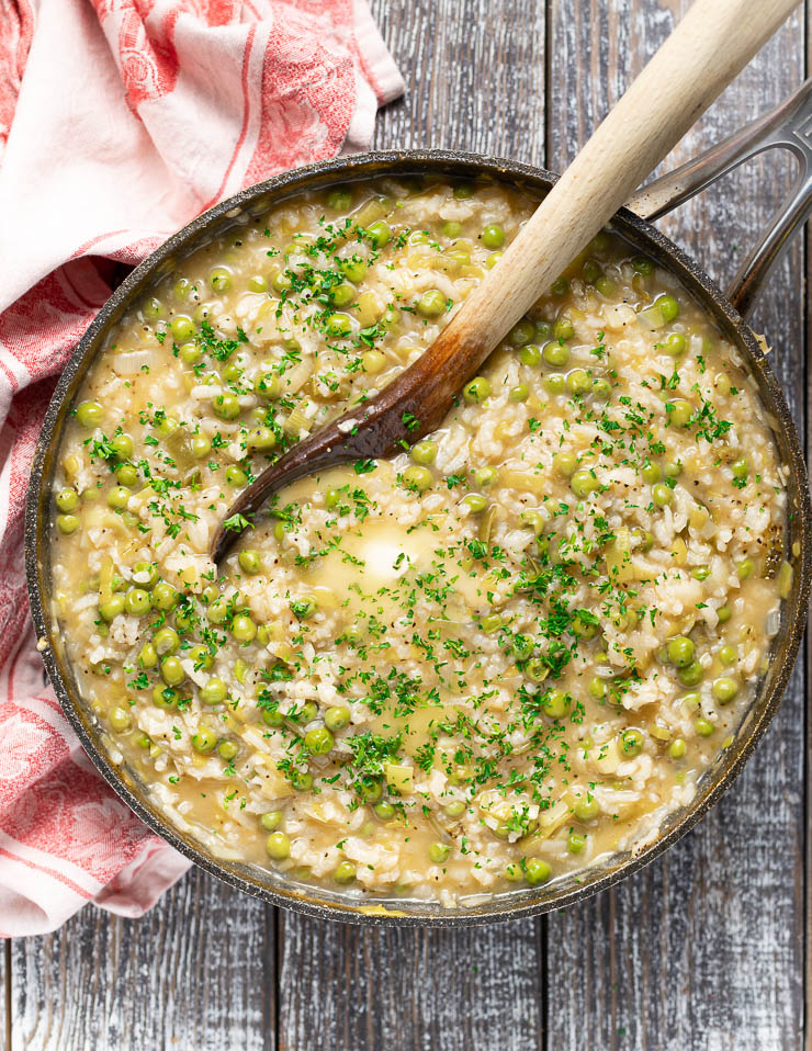 Photo of a large pot of Italian rice and peas being served with a large wooden spoon. One of the family favorites out of the vegan Italian Recipes.