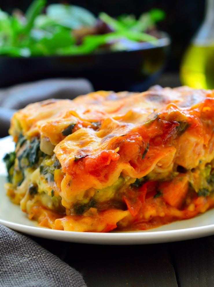 Photo of vegan lasagna being served on a white plate with a garden salad in the background. This is a stand out classic among the vegan Italian recipes.