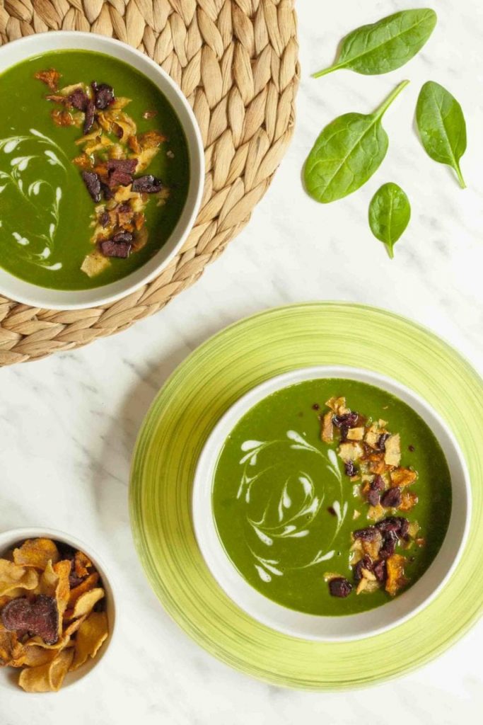 Photo of two bowls serving cream of spinach soup. A side of kettle chips is also seen in the photo. 