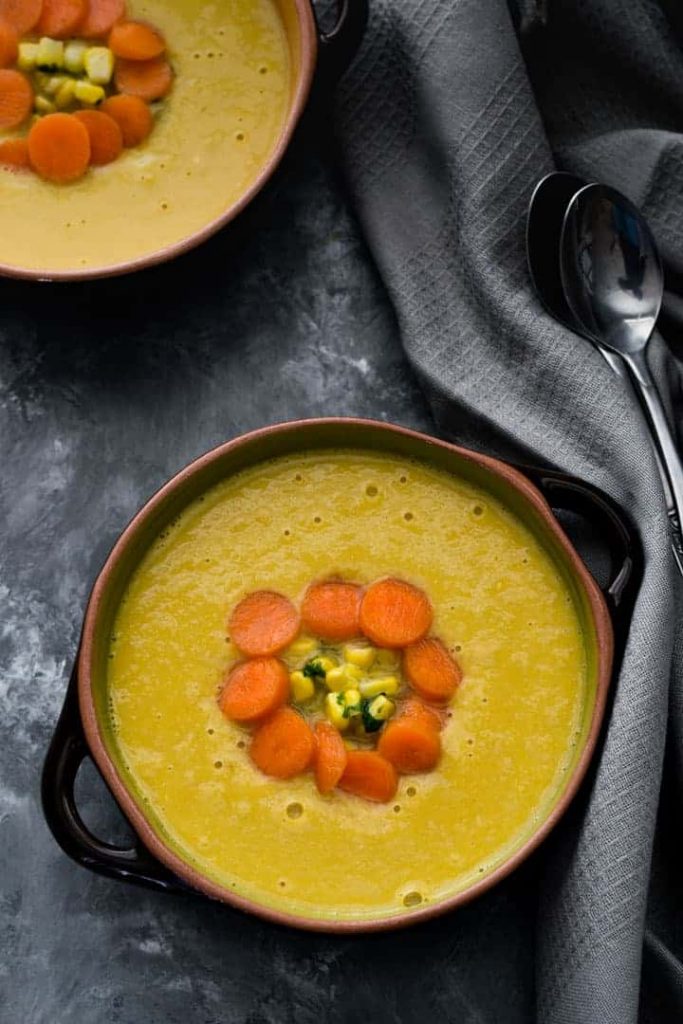 Photo of two bowls of Indo-Chinese Corn soup with two silver spoons and a gray cloth napkin.