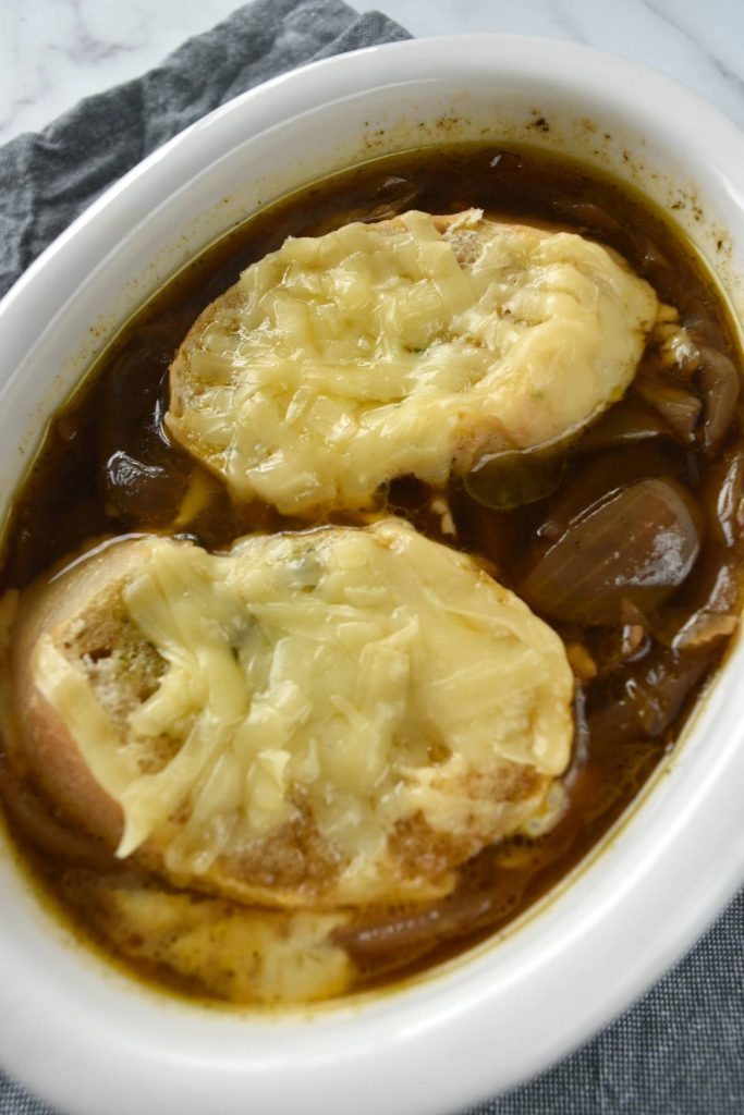 Photo of slow cooker french onion soup being served in a white bowl. A favorite among the vegan soup recipes. 