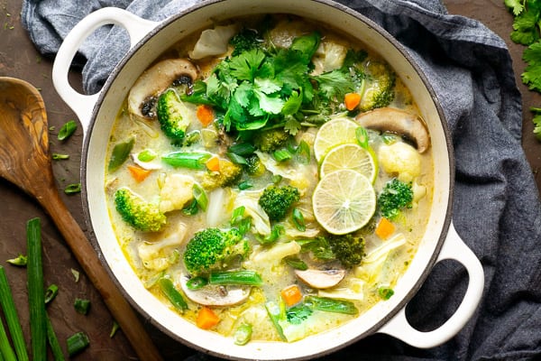 Photo of a large pot of thai coconut soup with a large wooden spoon.