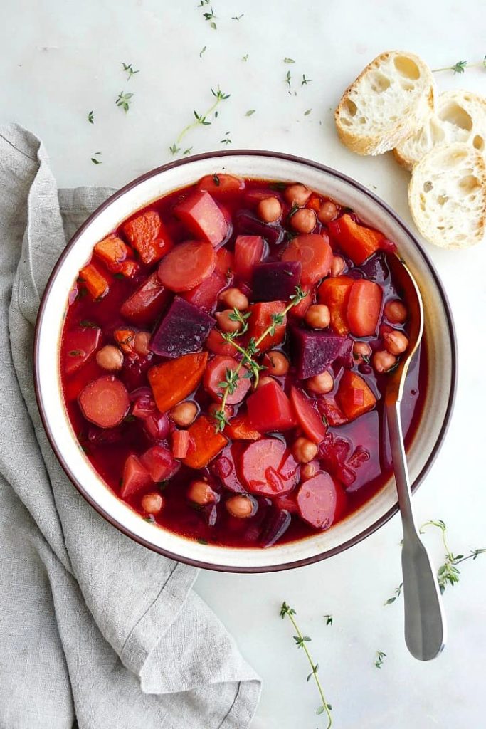 Photo of vegan stew with winter vegetables being served in a round bowl with a side of sliced bread. 
