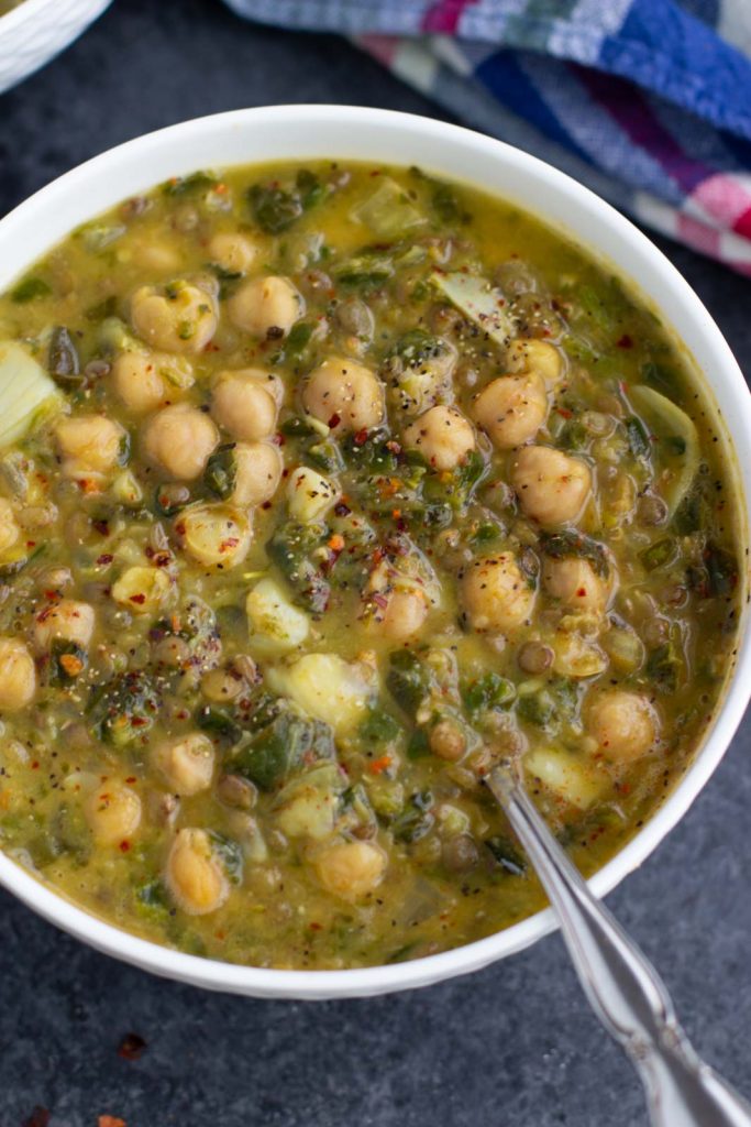 Photo of Creamy Coconut Lentil Chickpea Spinach Soup being served in a round white bowl.