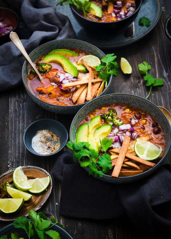 Photo of three bowls serving Dump & Start Red Lentil Tortilla Soup. Cilantro and lime are on the side as a garnish.