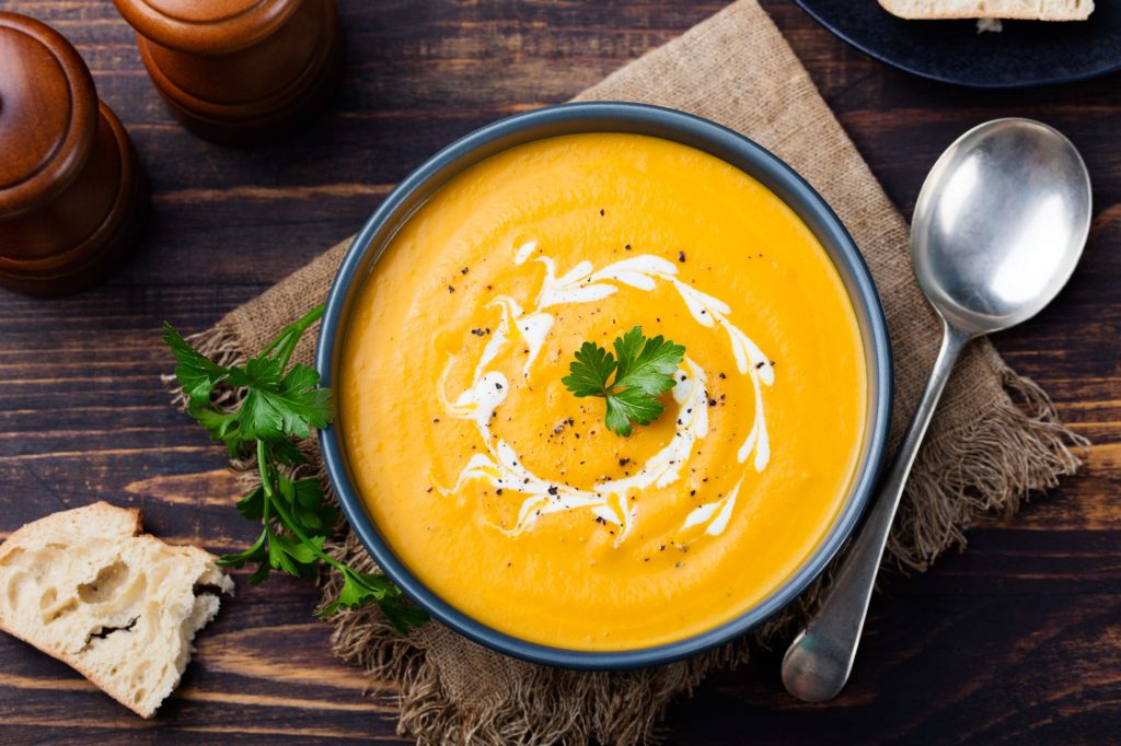 Photo of a bowl of Pumpkin and carrot soup, tadka with cream and parsley on dark wooden background.