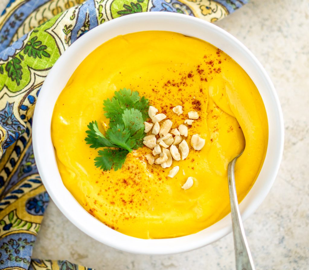 Photo of vegan sweet potato peanut soup being served in a white round bowl with a colorful cloth napkin.