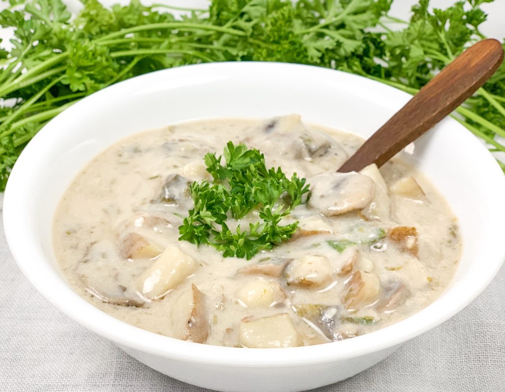 Photo of vegan clam chowder being served in a white round bowl with a wooden spoon.