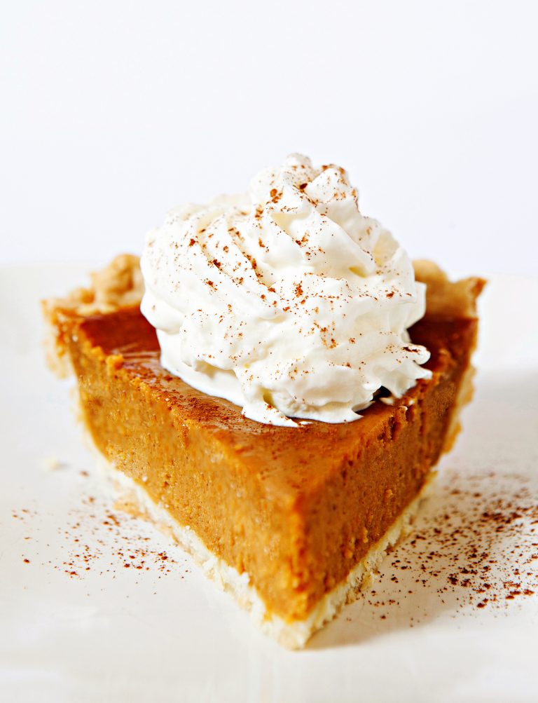 Photo of a slice of vegan thanksgiving pumpkin pie topped with whipped cream and cinnamon.